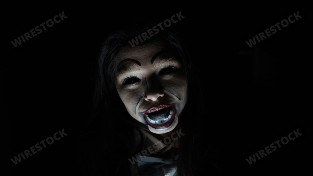 A scary possessed girl with a creepy doll makeup in a dark room - horror concept
