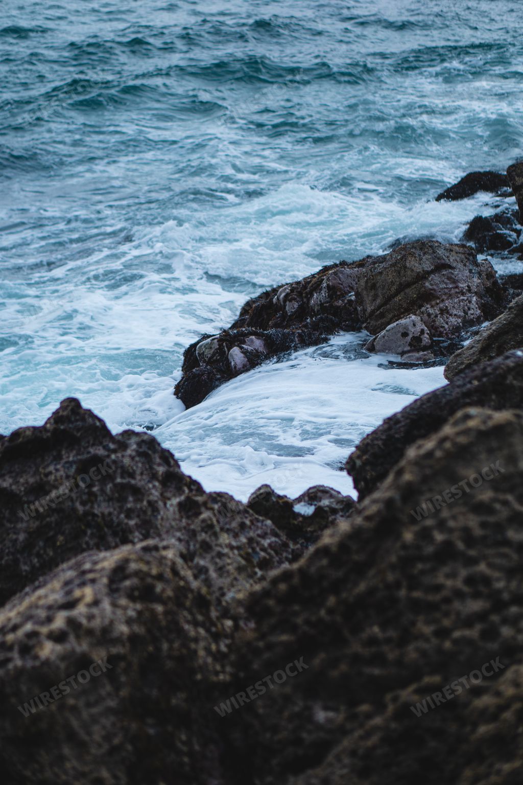 A vertical shot of waves crashing on the rocks on the coast