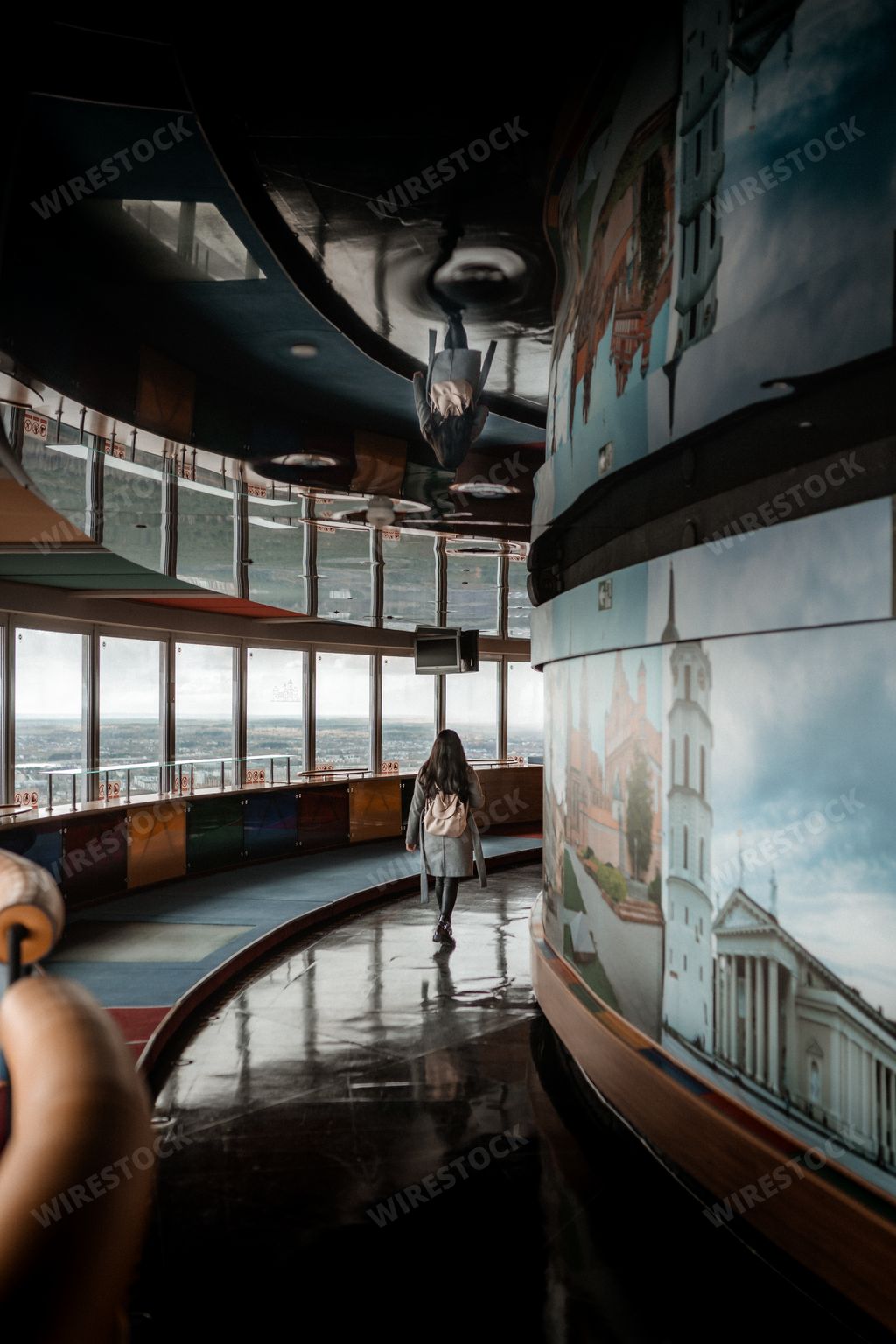 A young girl with a backpack from behind walking on reflective floors in a curving hallway with mural paintings on the wall next to her