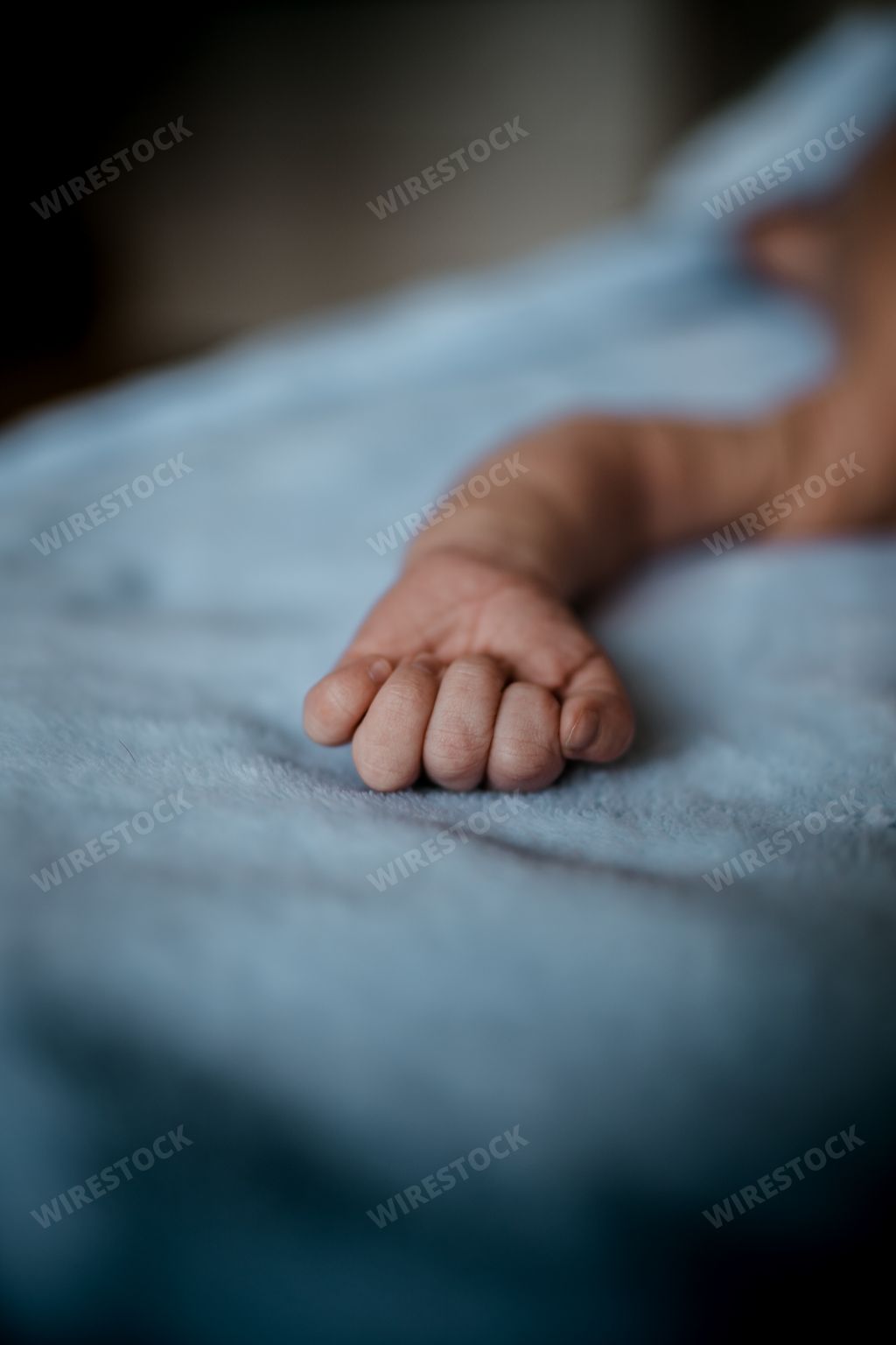 A vertical closeup shot of a baby hand laying on the bed. Cute baby fingers, perfect for wallpaper