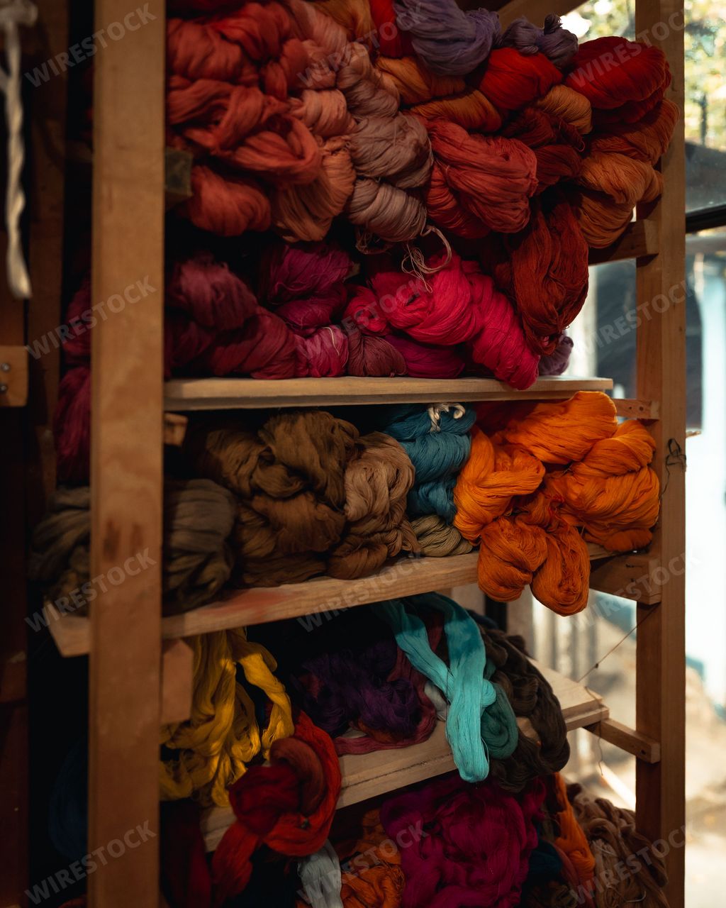 A vertical shot of colorful wool yarns sorted on a wooden shelving unit