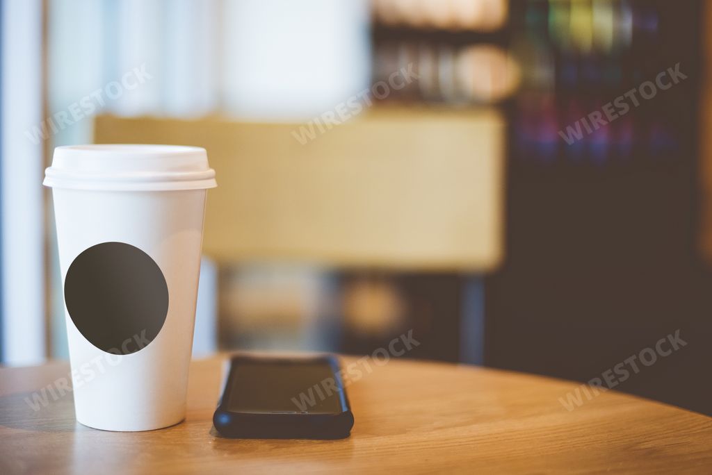 A closeup shot of a coffee near a smartphone on a wooden table with a blurred background
