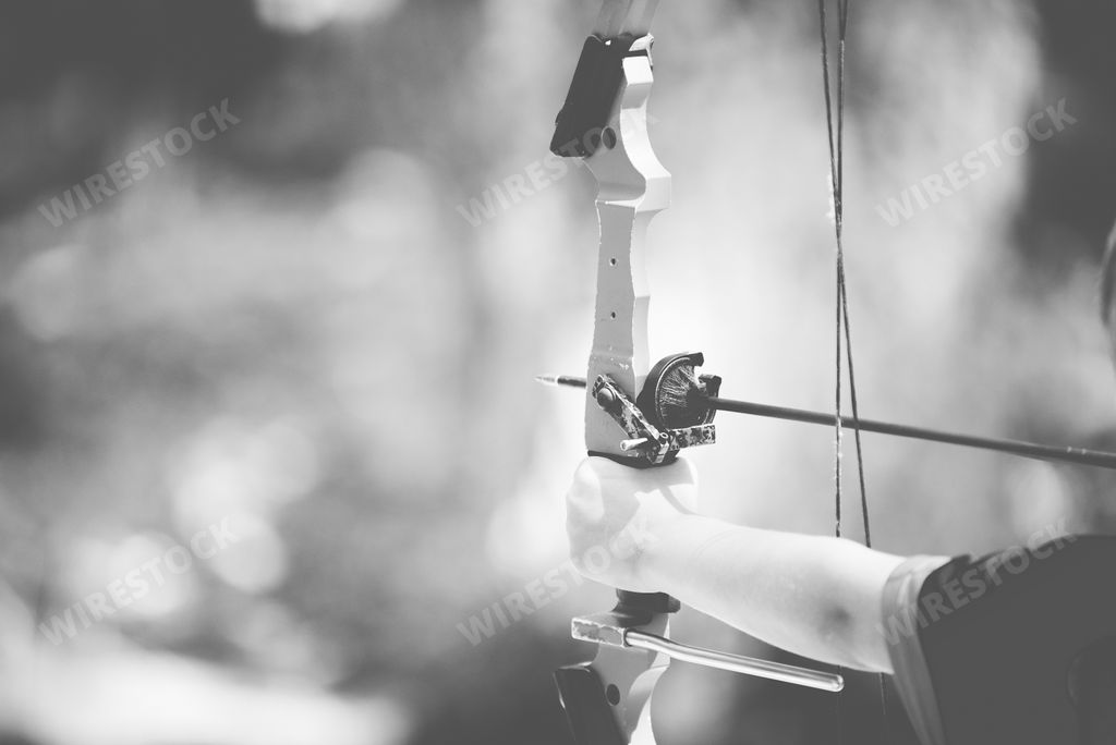 A closeup shot of a person holding a bow and arrow with a blurred background in black and white