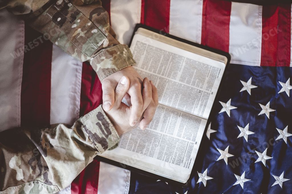 An American soldier mourning and praying with the Bible in his hands and the American flag