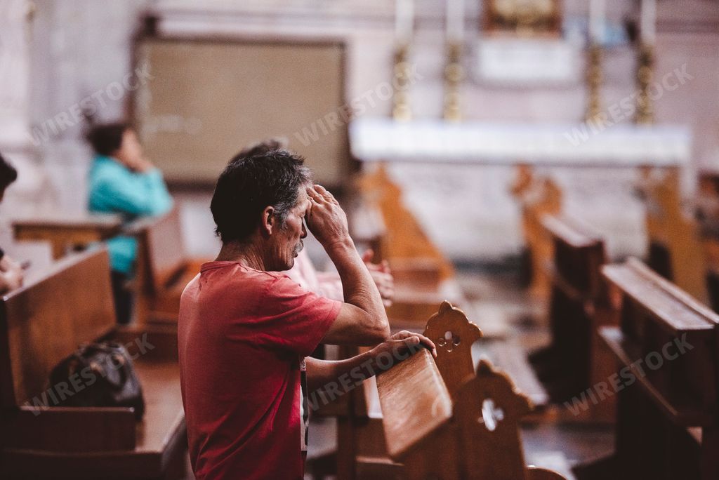 A shallow focus of a Hispanic man kneeling in prayer in a church at Zacatecas, Mexico