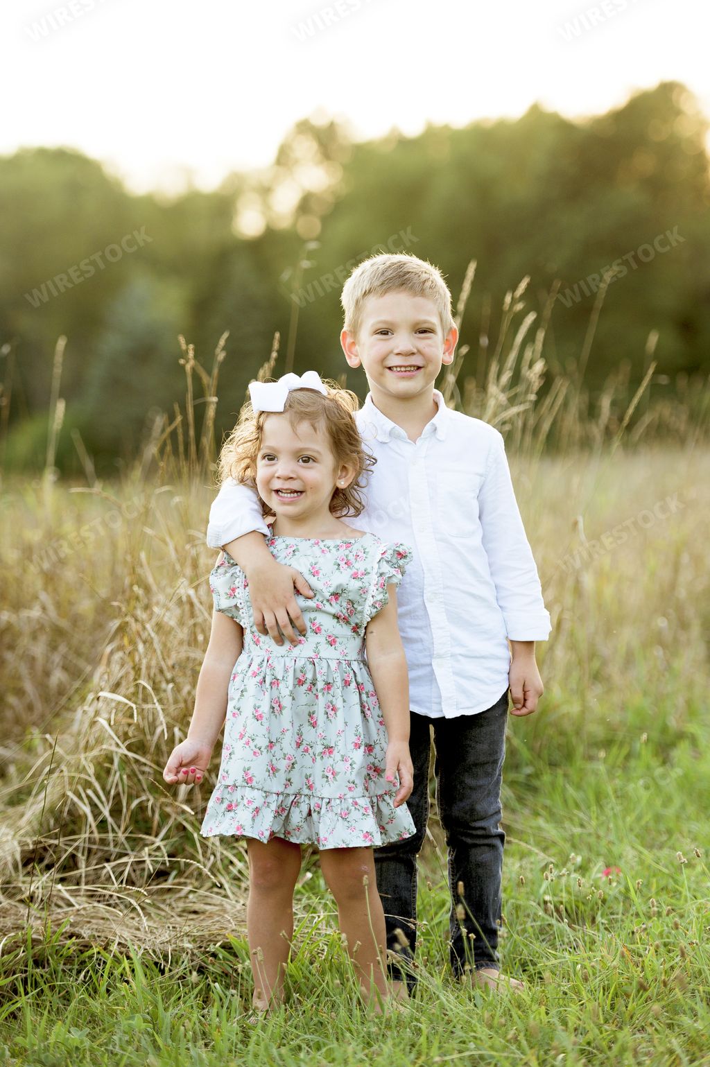 A vertical shot of a little brother hugging his sister while standing in a grassy field