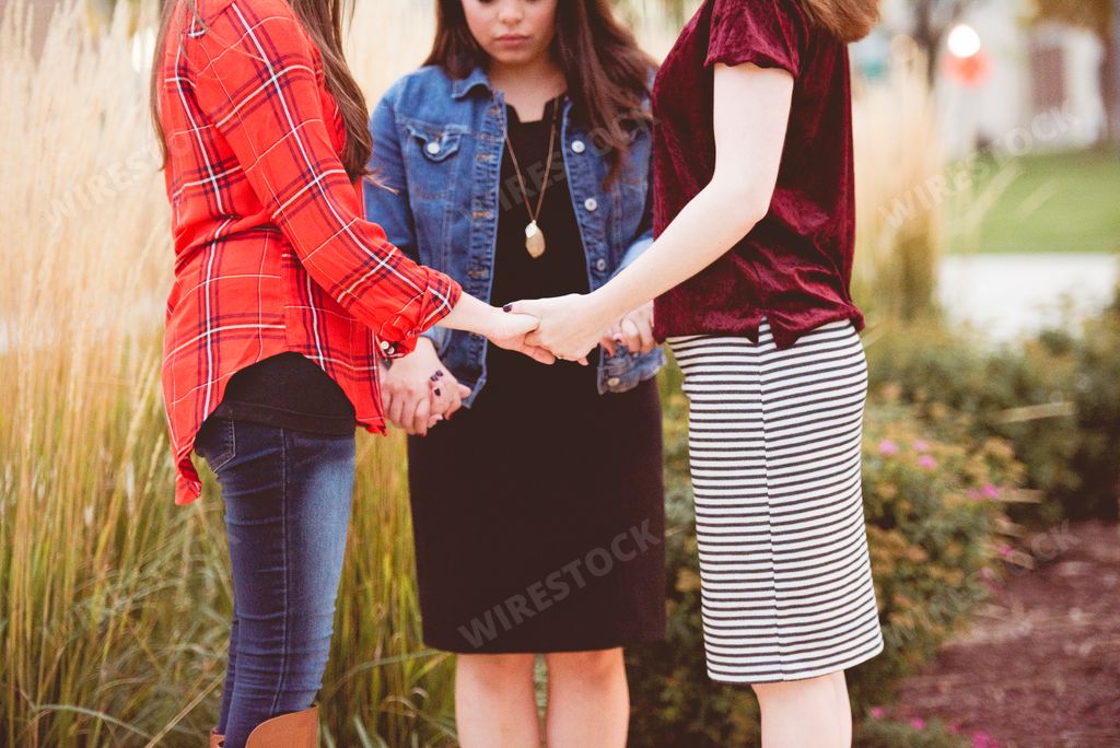 A group of young women holding hands and praying together in the park during Bible study