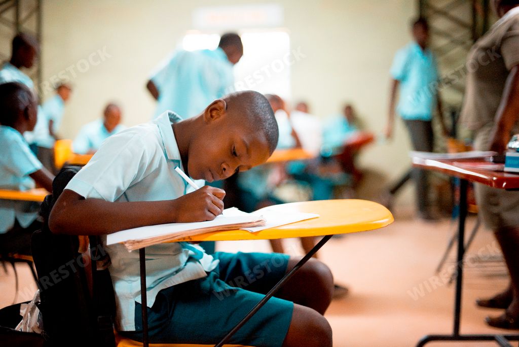 A shallow focus of a black boy writing at class with his classmates in the background at a school in Haiti