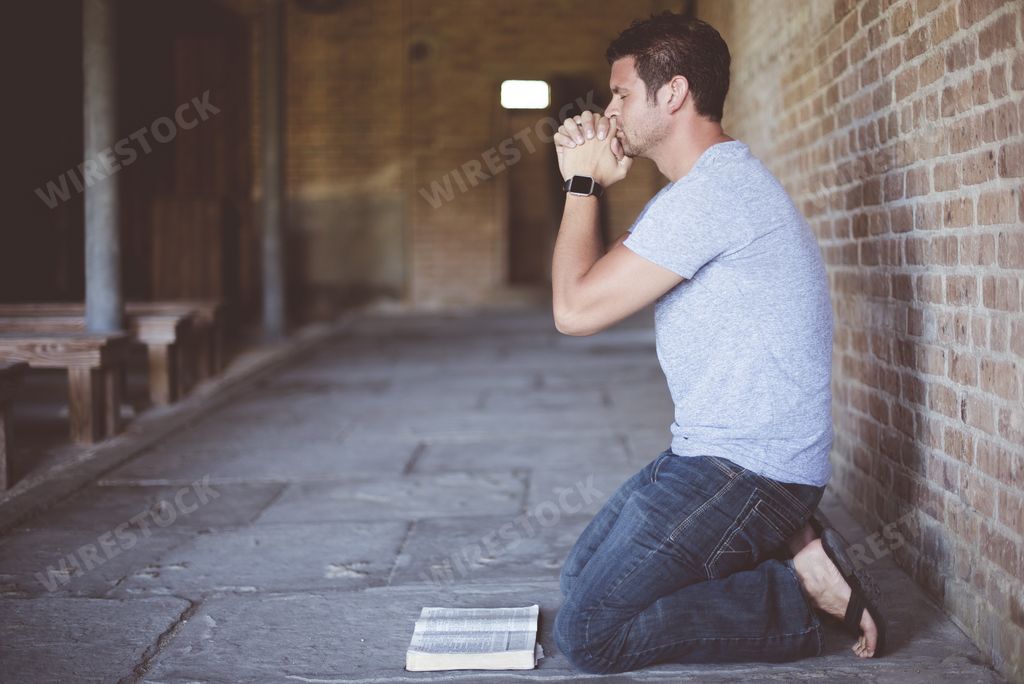 A closeup shot of a male on his knees with an open bible in front of his while praying