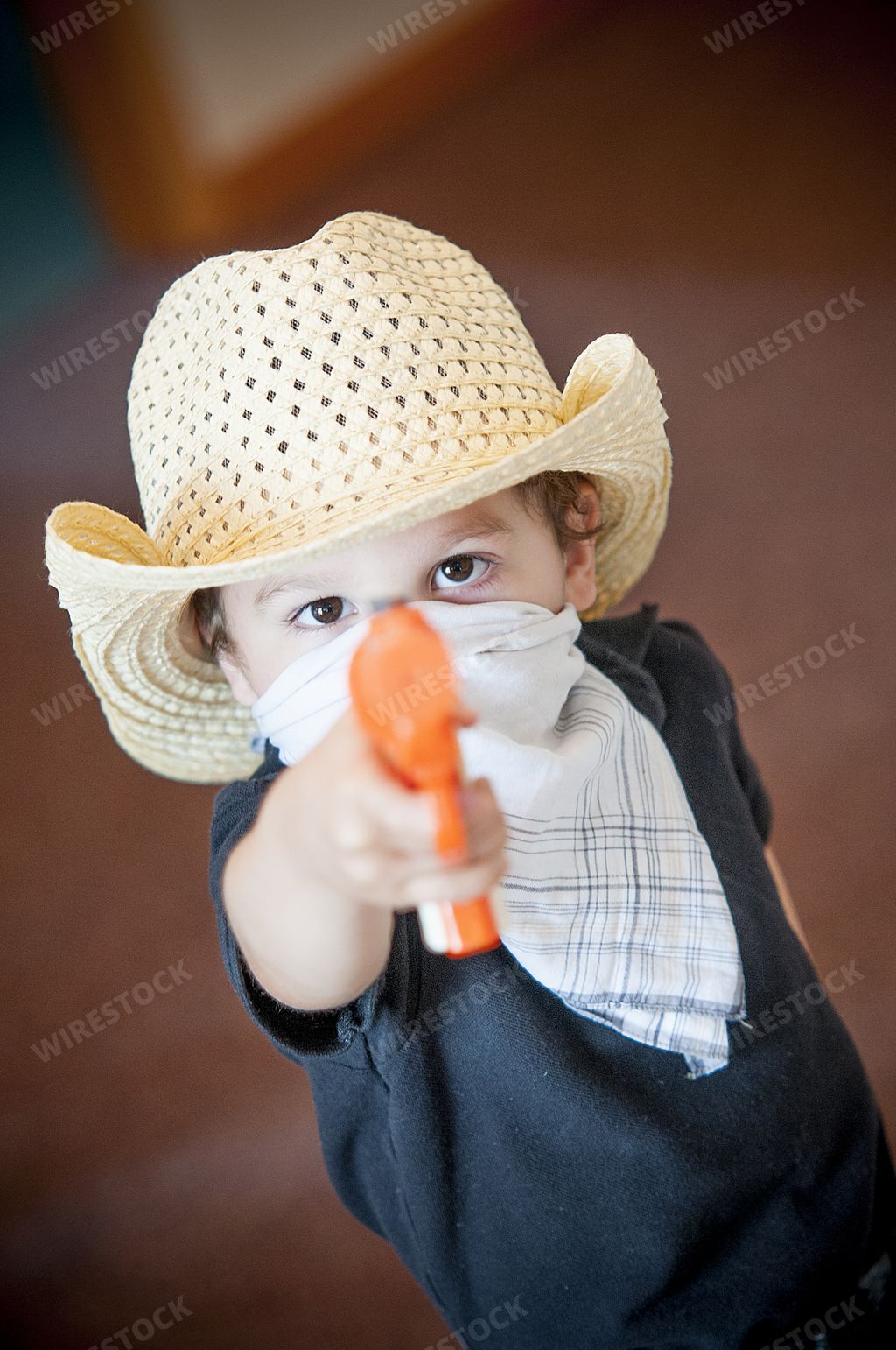A vertical shot of a kid with a toy gun, hat, and a handkerchief posing as a gunman