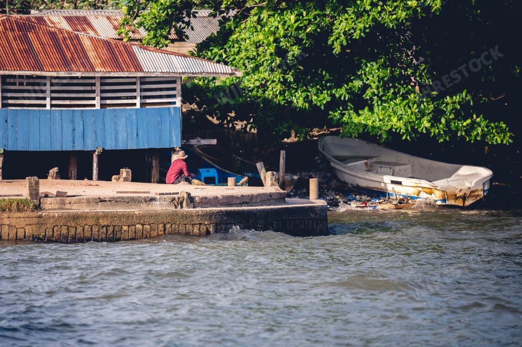 A man sittin on the coast near its house and a dirty boat in Puerto Lempira, Honduras