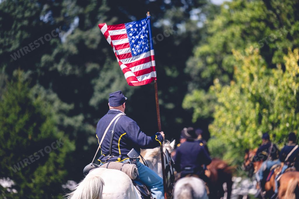 A veteran riding a horse and holding the USA flag reenacting the American Civil War.