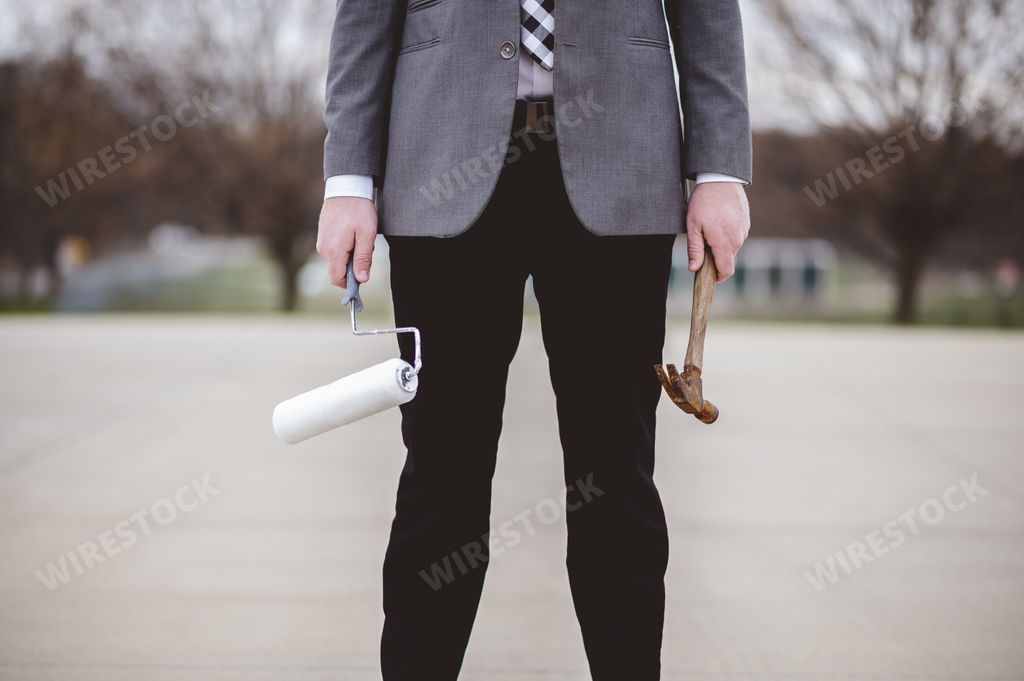 A shallow focus shot of a male holding a wooden hammer and a painting brush on the street