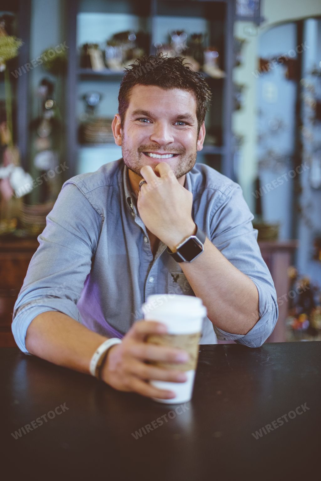A vertical shot of a male sitting in a cafe with a coffee and smiling at the camera