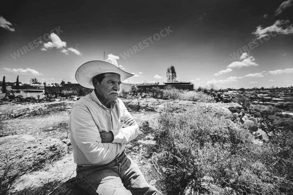 A grayscale shot of an old Hispanic with a cowboy hat sitting alone at a field in Zacatecas, Mexico