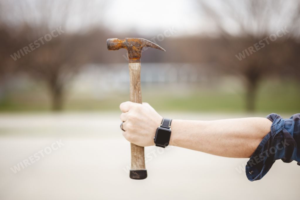 A man holding out an old rusty hammer against a blurry background