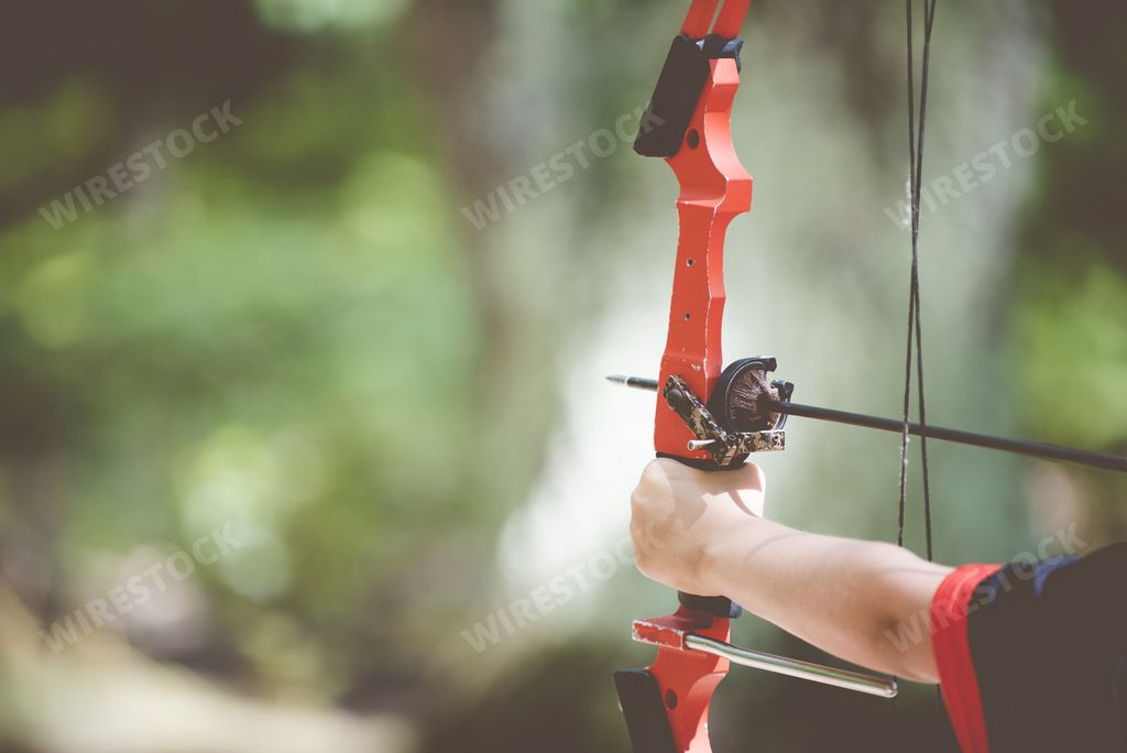 A closeup shot of a person holding a bow and arrow with a blurred background
