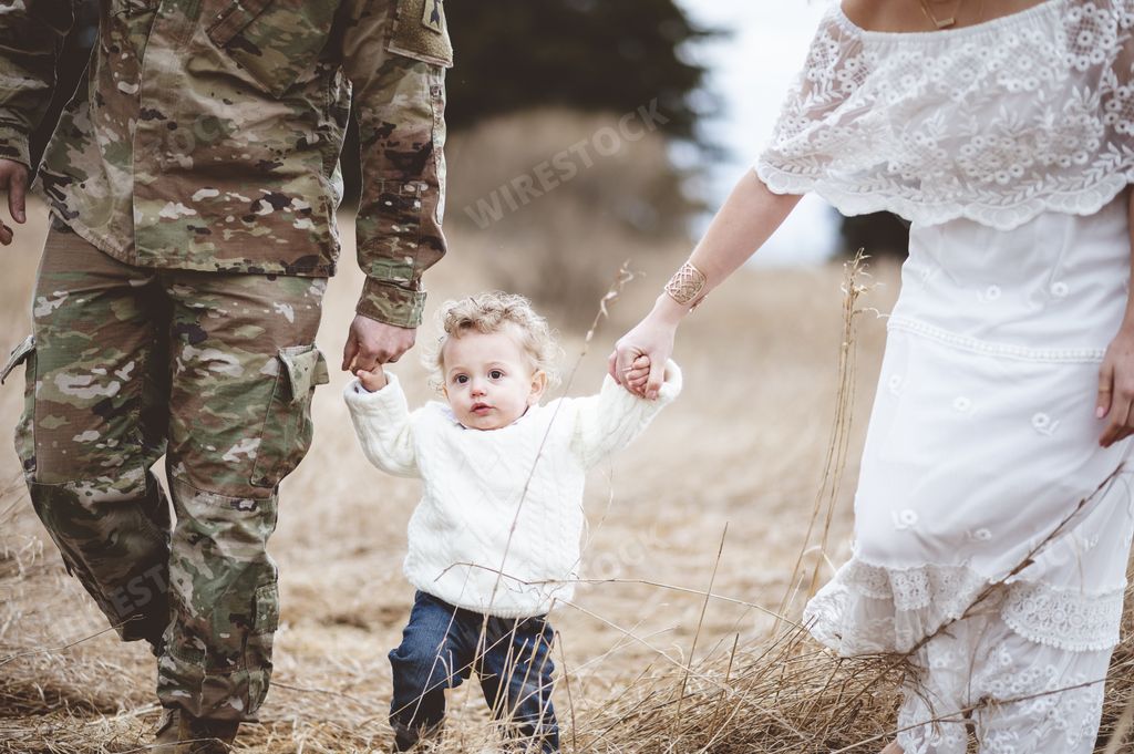 A soldier father with his wife holding the hands of their son from both sides and walking in a field
