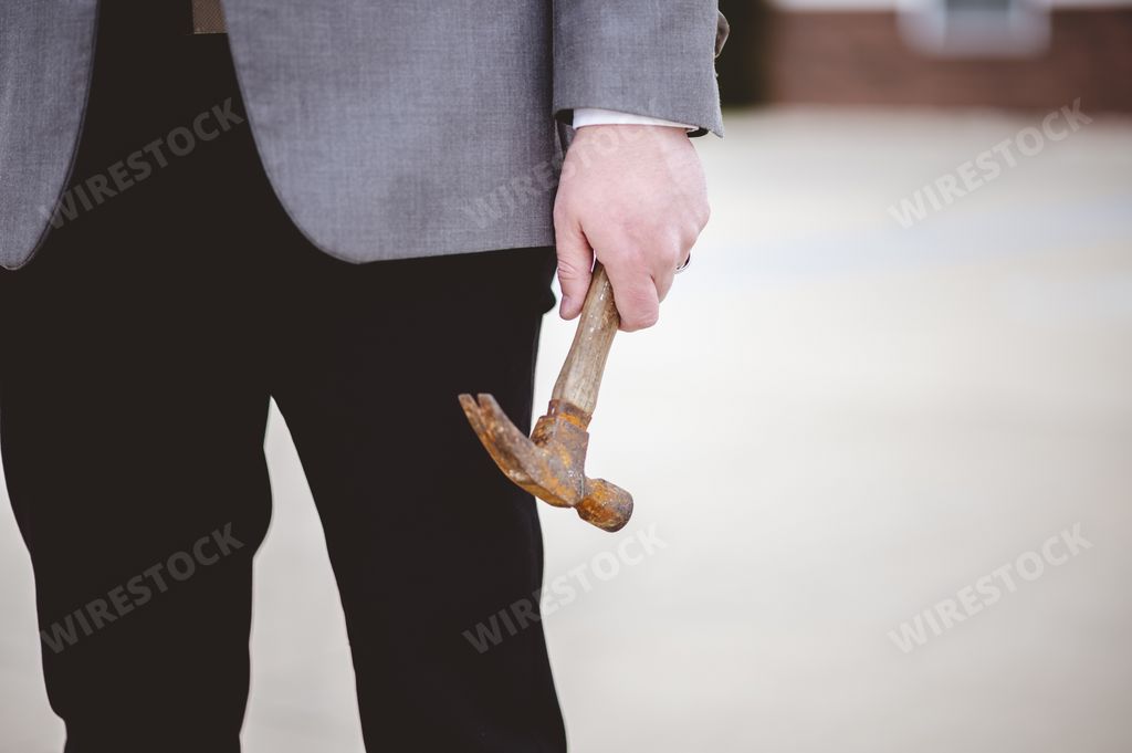 A closeup of a male in a suit and holding an old wooden hammer while standing outdoors