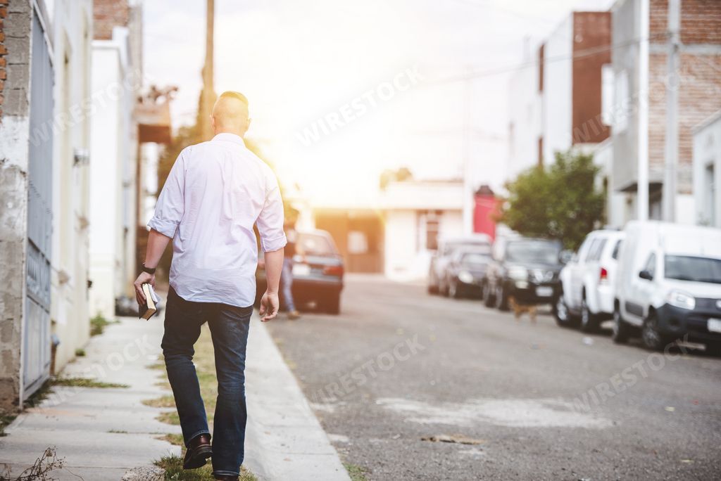 A closeup shot from behind of a male walking on the sidewalk while holding the bible