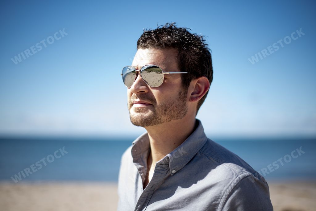 A shallow focus shot of a male wearing sunglasses at the beach on a sunny day