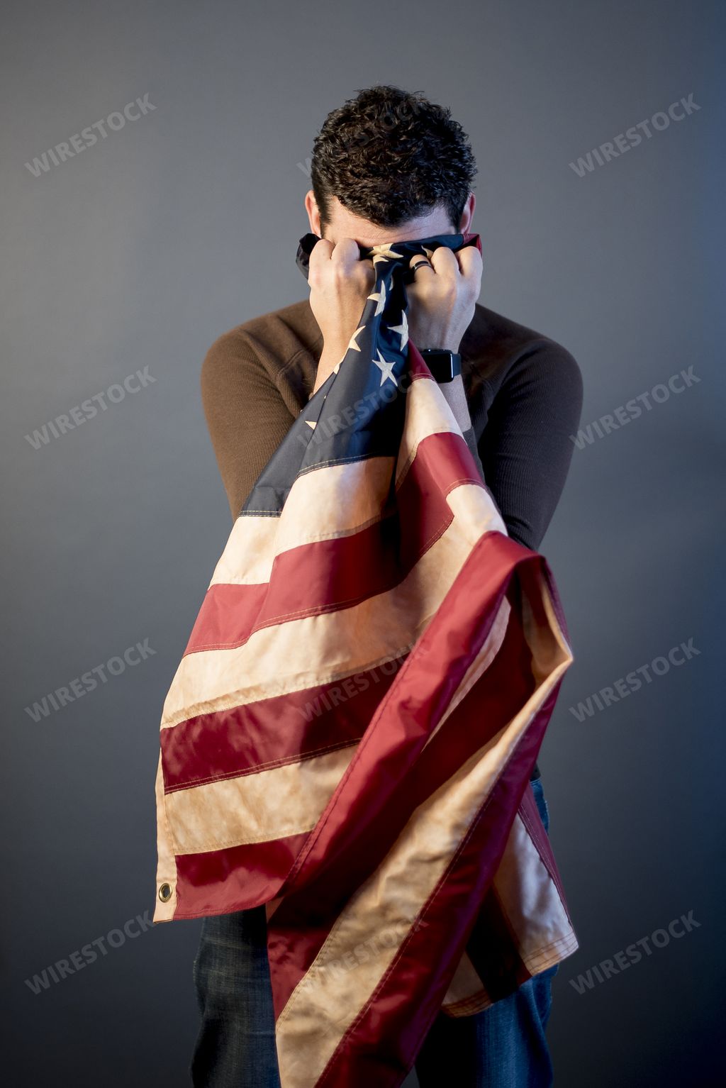 A vertical shot of a retired soldier crying in grief and cleaning his tears with the united states flag