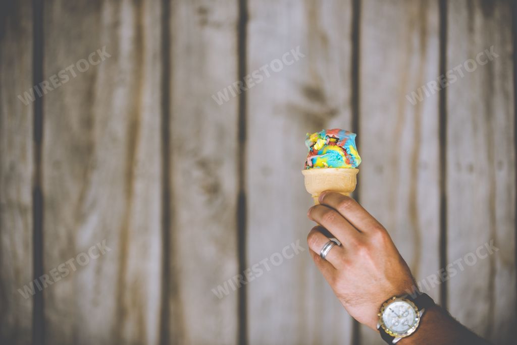 A closeup shot of a male hand holding a colorful ice cream  on a wooden background - childhood is back concept