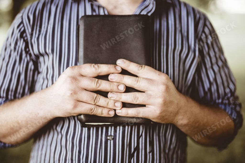A closeup shot of a male holding the bible against his chest with a blurred background