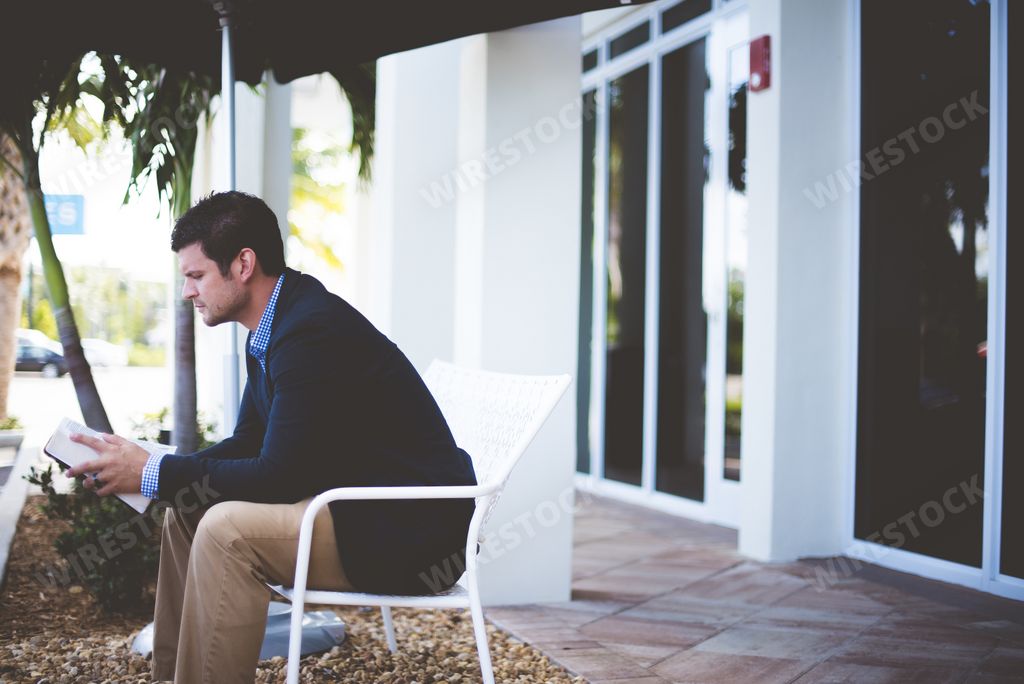 A well-dressed male sitting and reading the bible with a blurred background