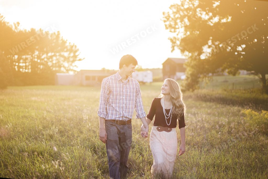 A couple holding hands in a garden surrounded by greenery under sunlight with a blurry background