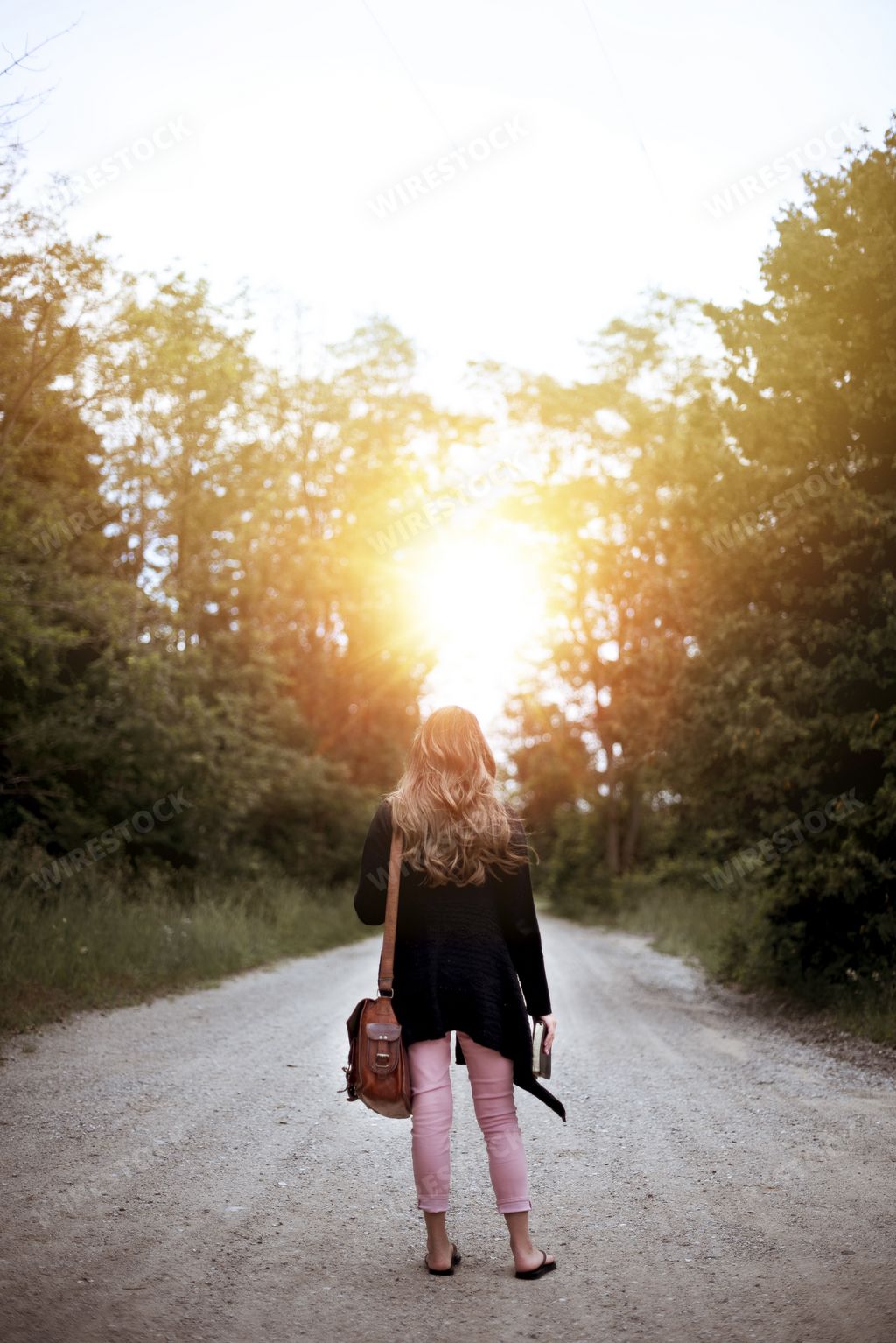 a vertical shot from behind of a female standing on an empty road while holding the bible