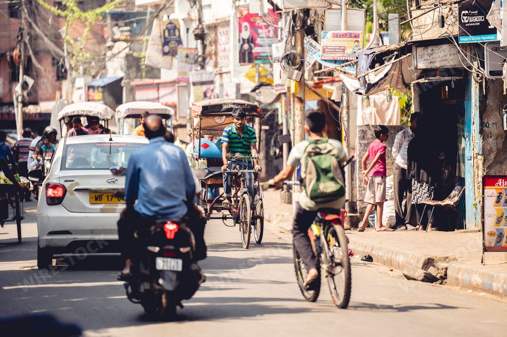 Indian people driving bikes, cars and walking down the street in a village in Kolkata, India