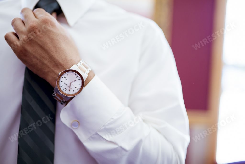 Man fastening his tie with a fancy watch on