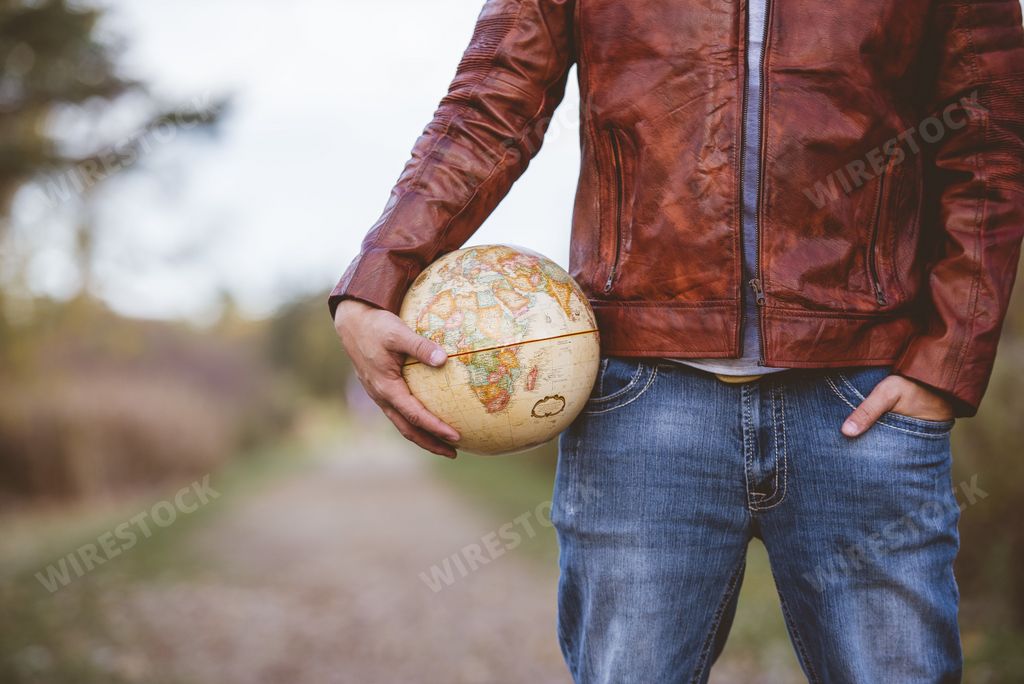 A closeup shot of a male wearing a leather jacket holding a desk globe with a blurred background