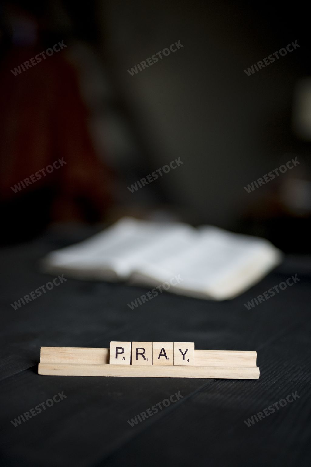 A vertical shot of wooden blocks spelling pray on a black wooden surface with a blurred background