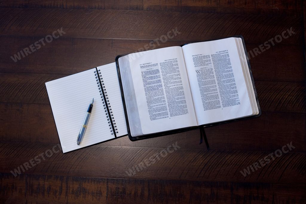 An overhead shot of an open bible near a notebook on a wooden surface