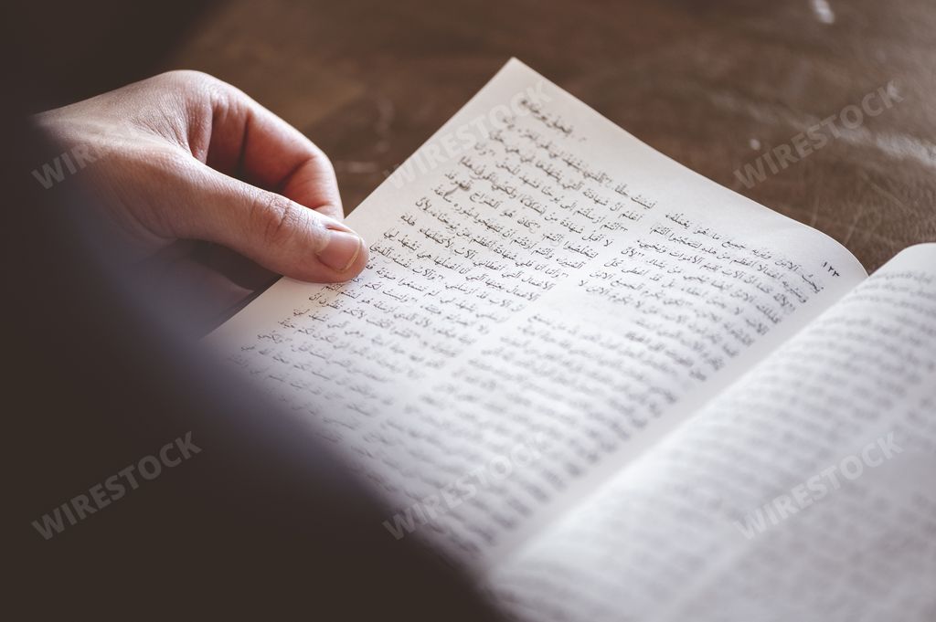A selective focus shot of a person reading an Arabic book on the table