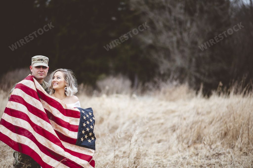 A shallow focus shot of an American soldier with his smiling wife wrapped in an American flag