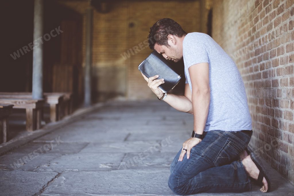 A closeup shot of a male down on his knees with the bible against his head while praying