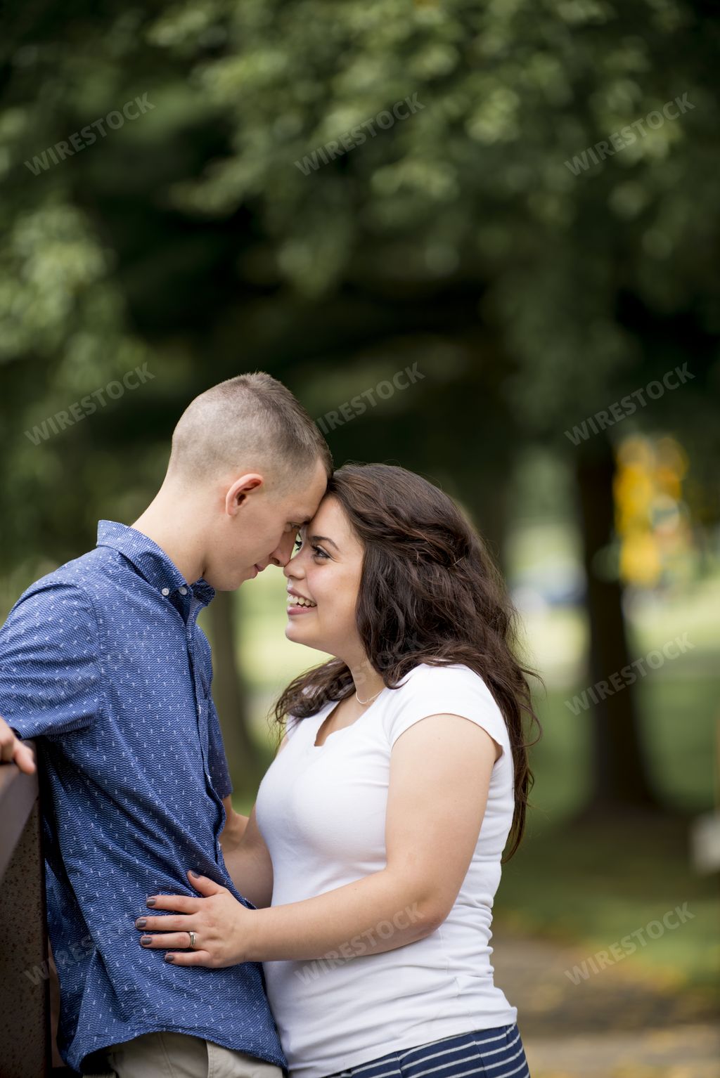 A couple touching foreheads in a park under sunlight with a blurry background