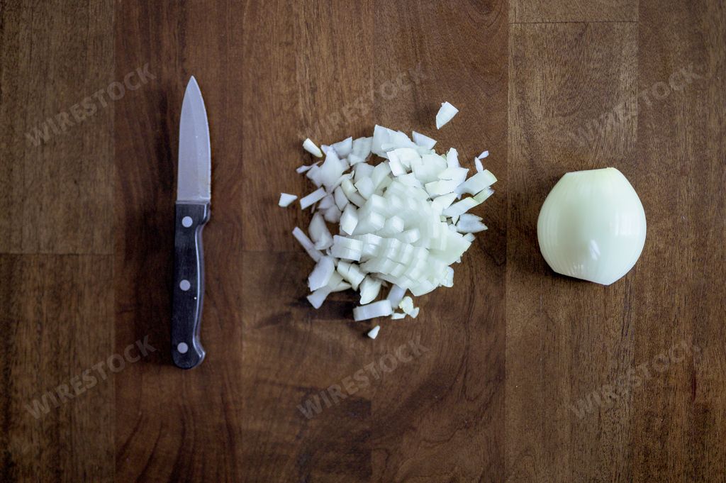 An overhead shot of a knife near chopped and sliced onion on a wooden surface