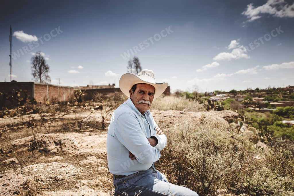 Shot of an Old Mexican Cowboy sitting on a rock with denim shirt in the desert