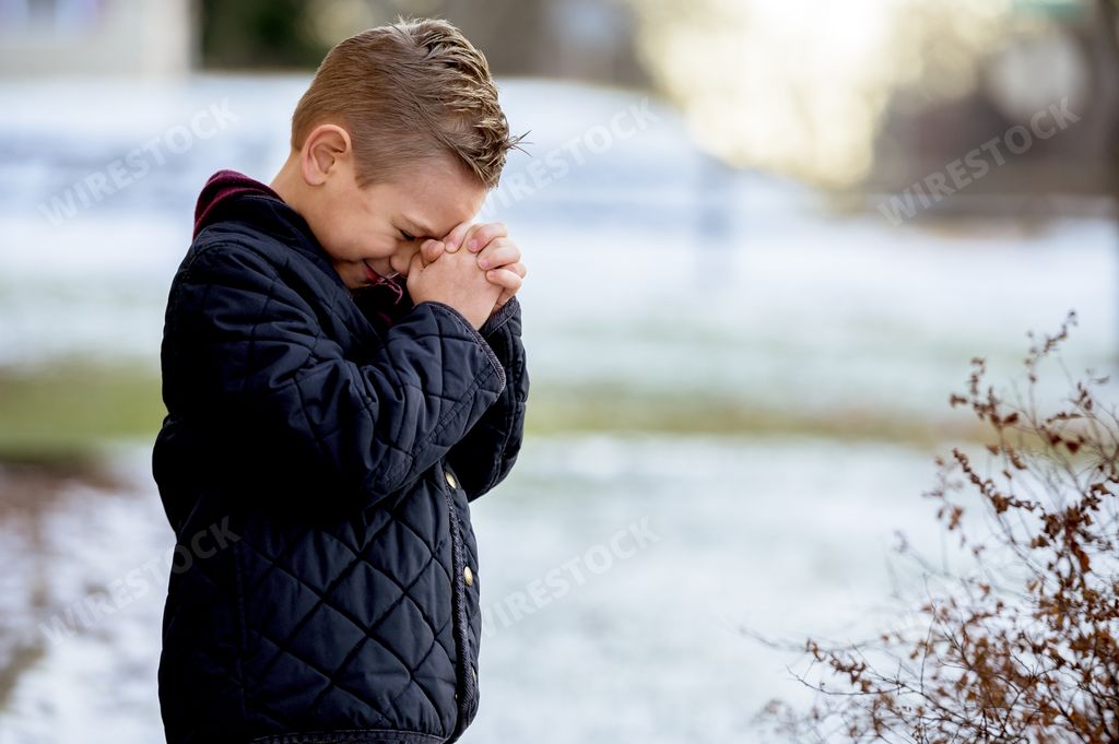 A boy standing with closed eyes and praying