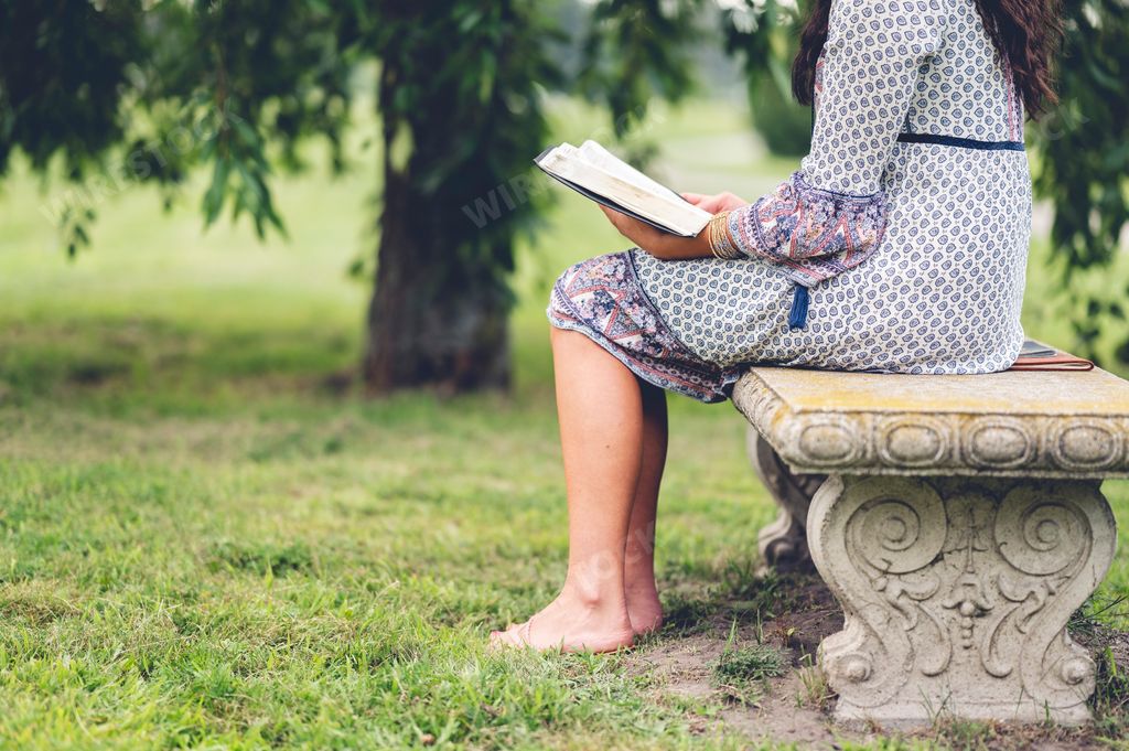 A detail of a lonely female sitting on a park bench with a book