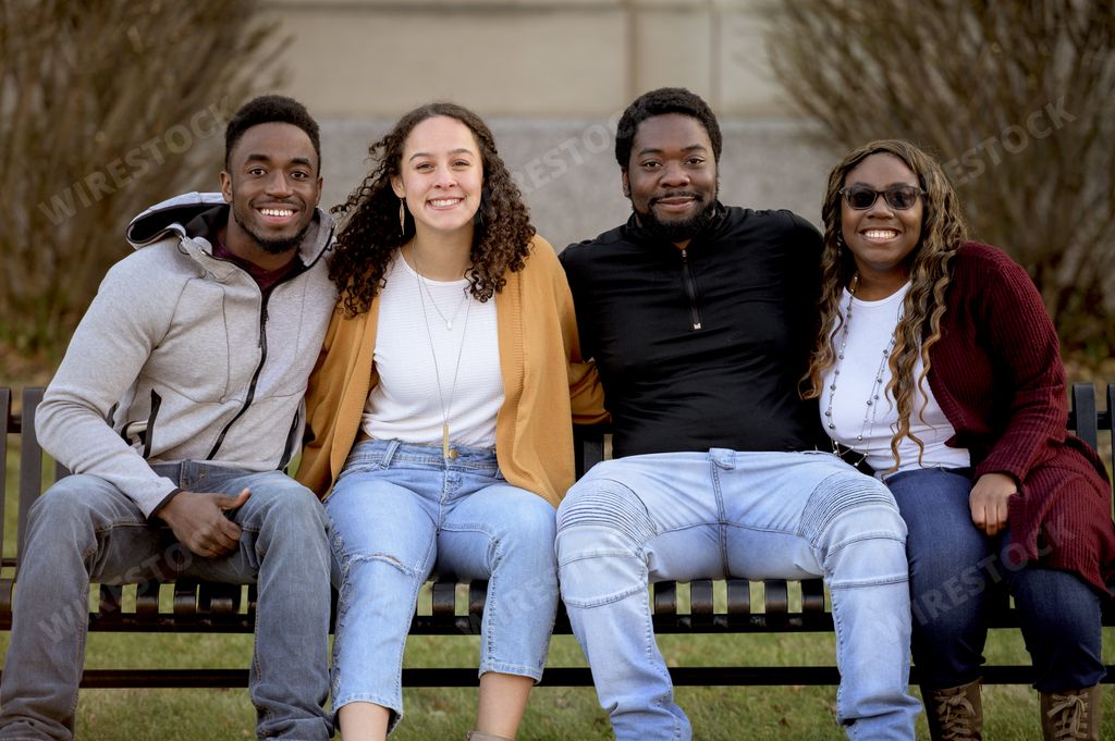 A group of people sitting on a bench in a park under sunlight with a blurry background