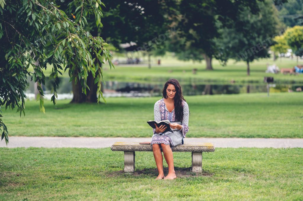 A young Caucasian man reading the Bible while sitting on a bench