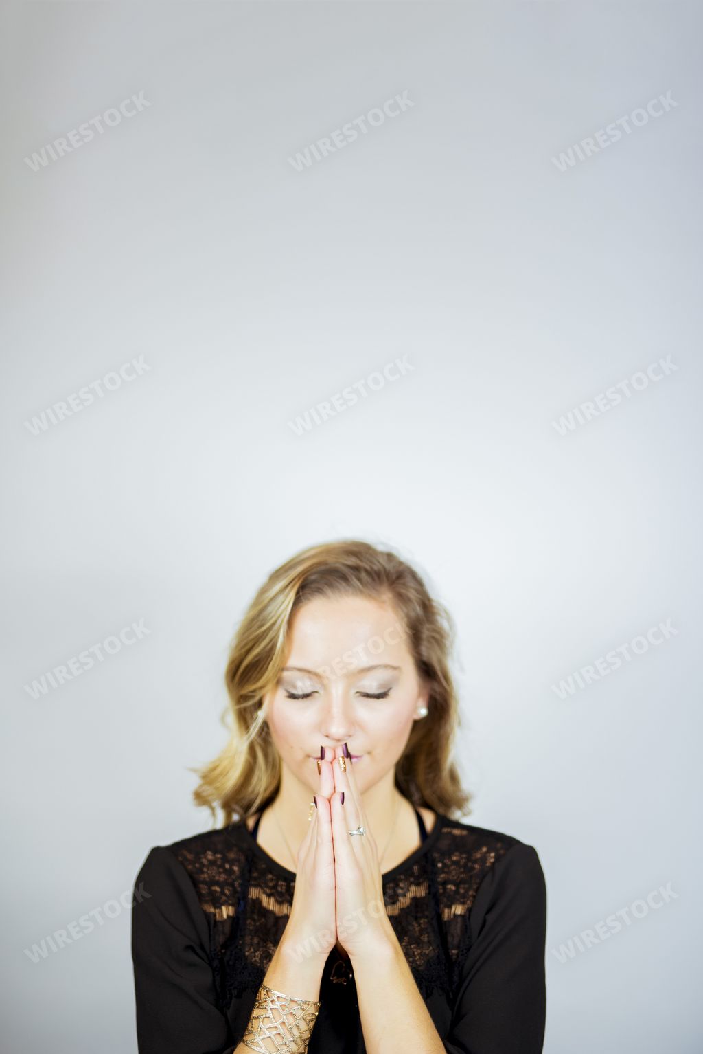 A vertical picture of a woman praying with her eyes closed against a white background