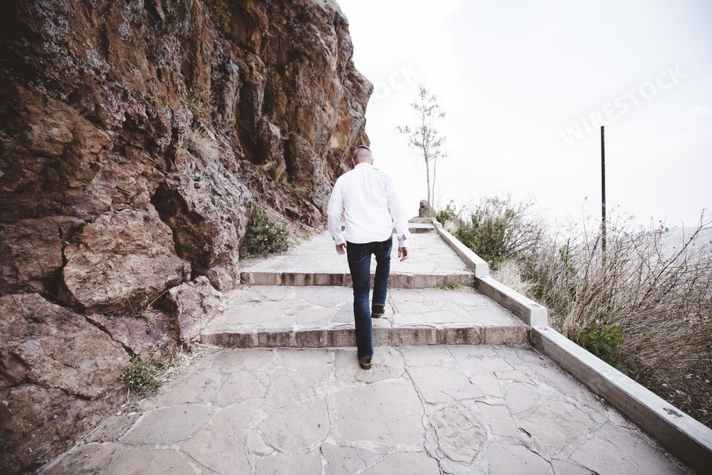 A male walking up the pathway on the side of a mountain shot from behind