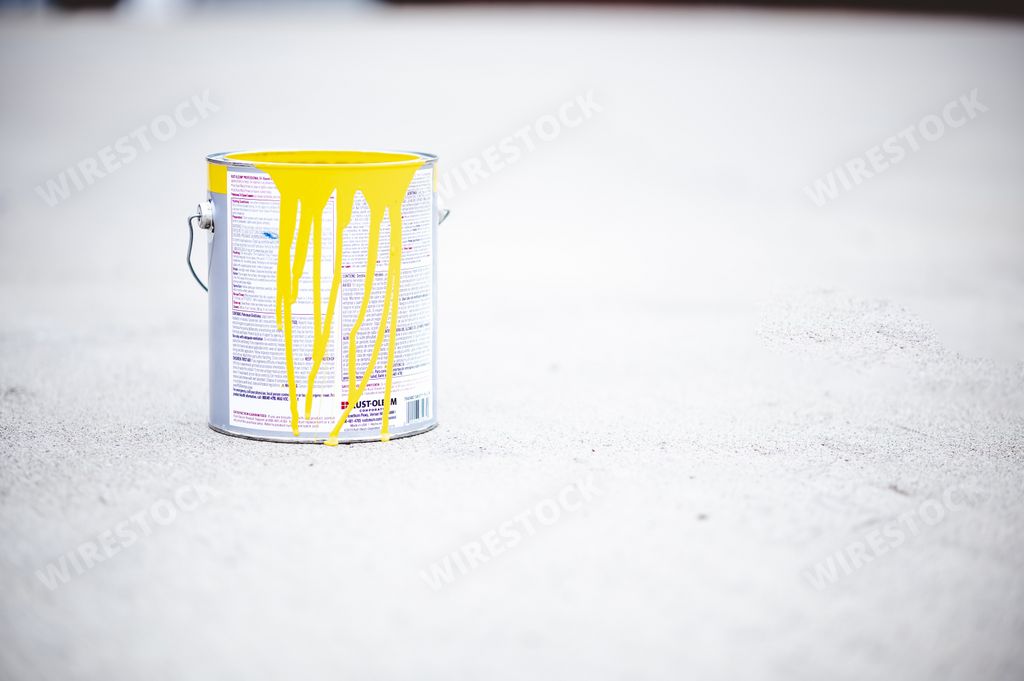 A view of a metal can with yellow paint on it placed on the asphalt of a street