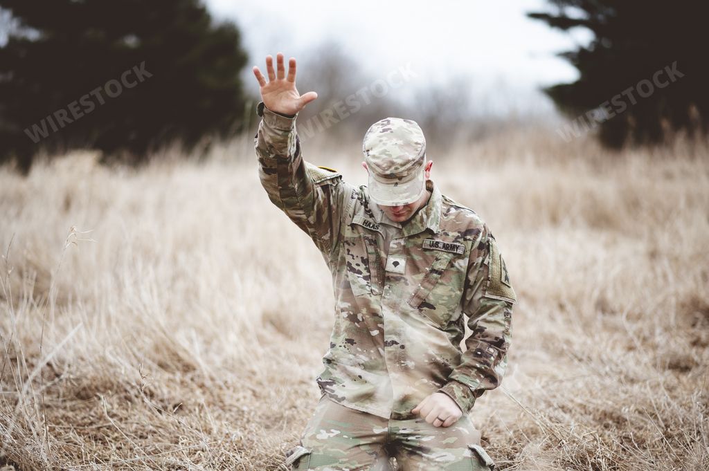 An American soldier kneeling in despair on a grass field with his hand raised above